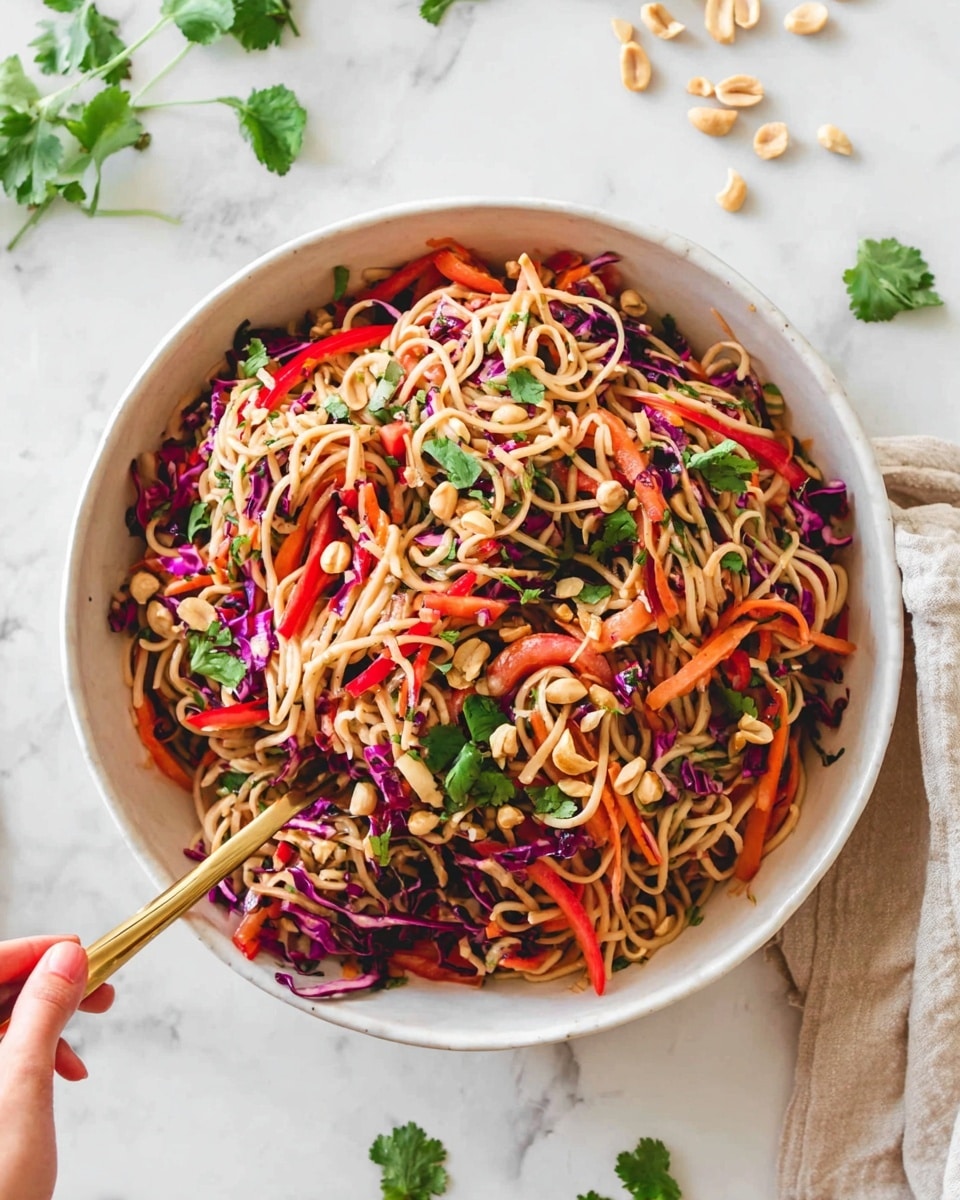 A large white bowl filled with a colorful noodle salad, showing several layers starting with light tan cooked noodles at the base, mixed with thin strips of bright red bell pepper and vibrant purple cabbage. Interspersed throughout are thin orange carrot sticks and fresh green cilantro leaves, with scattered whole and chopped light brown peanuts adding texture on top. A woman's hand holding a gold fork rests on the edge, ready to serve, all set on a white marbled surface with some peanuts and cilantro leaves scattered around. Photo taken with an iphone --ar 4:5 --v 7