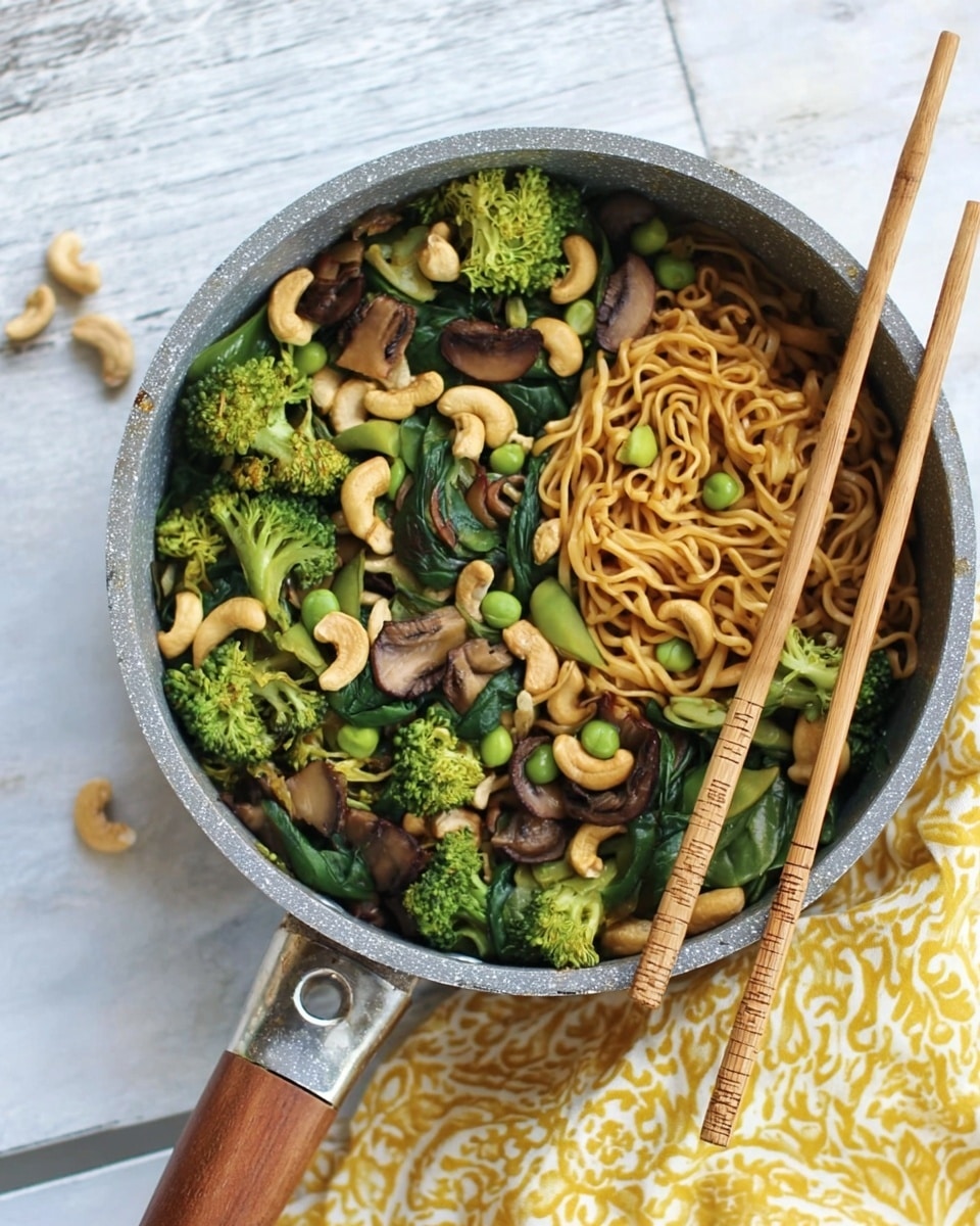 The image shows a grey pan filled with a colorful noodle dish on a white marbled surface. The first layer is light brown noodles, slightly glossy with sauce. On top of the noodles, there is a layer of green broccoli florets and leafy dark green spinach scattered across. Mixed in this layer are brown mushroom slices, pale cashew nuts, and small light green peas creating a varied texture. To the side of the pan, light wooden chopsticks rest on the surface, and a yellow patterned cloth is partly visible in the background. The photo is taken with an iphone --ar 4:5 --v 7
