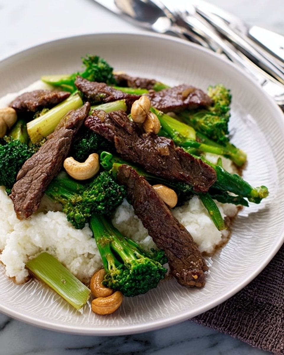 A white plate holds a dish with three main layers. At the bottom is a bed of white mashed potatoes, smooth and creamy. On top of that are several long strips of cooked beef, dark brown and slightly seared. Mixed around the beef are bright green cooked broccoli florets and light green celery pieces, adding color and texture. Scattered on the dish are a few toasted cashew nuts, light golden brown and shiny. The plate is set on a white marbled surface with a woman's hand nearby, and the background shows blurred shapes of silver cutlery. photo taken with an iphone --ar 4:5 --v 7