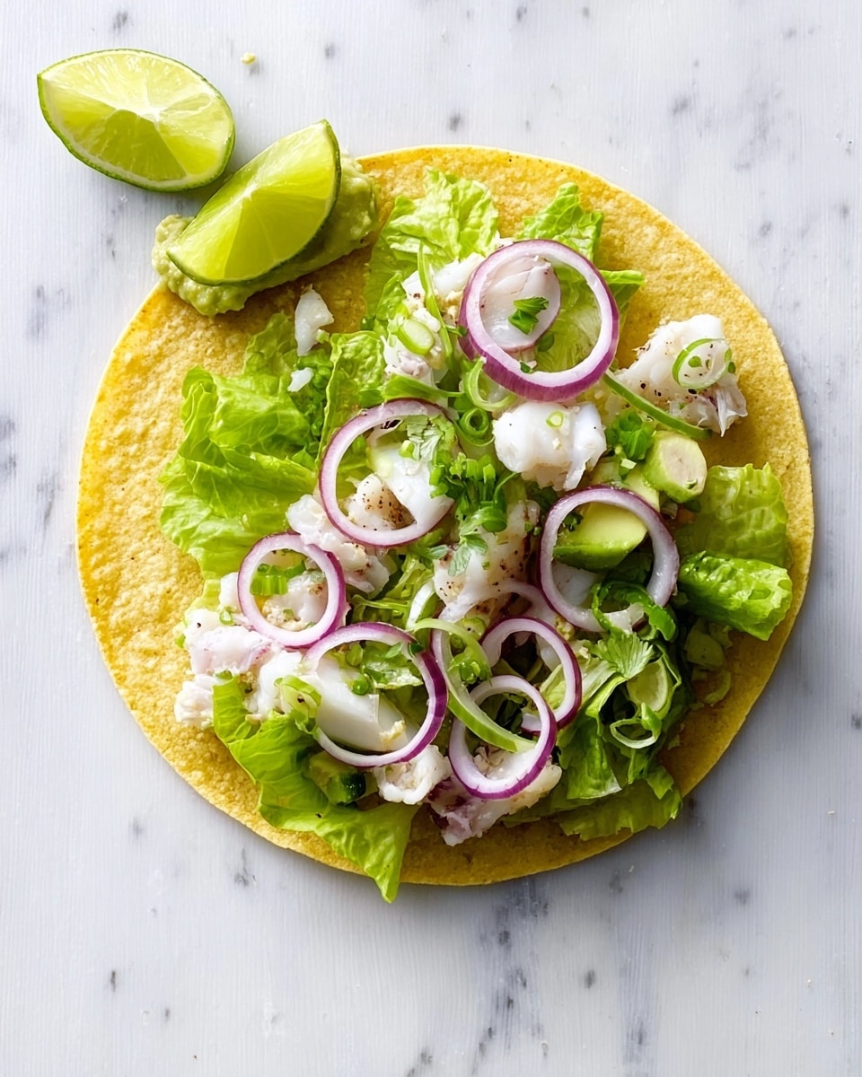 A single yellow corn tortilla laid flat on a white marbled surface, topped with a layer of green lettuce leaves, followed by scattered chunks of white fish. Thin rings of purple onion are placed on top along with small green onion slices. There are two lime wedges positioned on the left edge of the tortilla, and a small amount of guacamole sits near the top left. Photo taken with an iphone --ar 4:5 --v 7