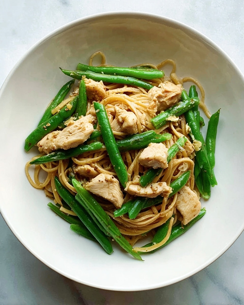 A white bowl holds a simple dish of yellow noodles mixed with cooked green beans and pieces of light brown chicken. The noodles are soft and curly, resting mostly at the bottom and middle of the bowl, with green beans and chicken chunks laid on top and between the noodles. The chicken pieces are irregular in shape, with a slightly shiny texture from cooking. The whole bowl sits on a white marbled surface, giving a clean, bright look. photo taken with an iphone --ar 4:5 --v 7