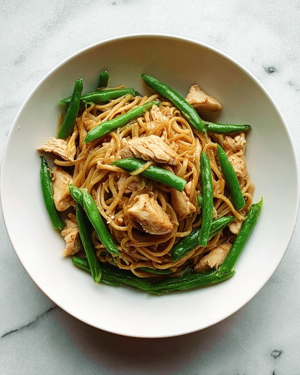 A white bowl holds a simple dish with three main layers: at the bottom are tangled, light brown noodles; on top of the noodles are bright green, cut green beans placed evenly around; and scattered over the green beans and noodles are light golden pieces of cooked chicken. The bowl sits on a white marbled surface. photo taken with an iphone --ar 4:5 --v 7