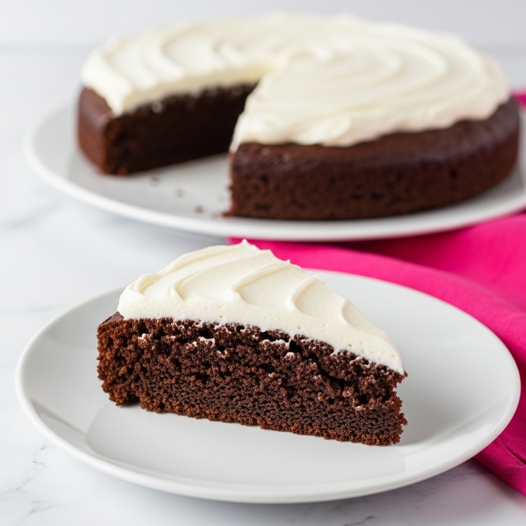 A slice of dark brown chocolate cake with a thick layer of smooth white frosting on top, showing a moist and soft texture. The cake slice sits on a white plate, placed on a white marbled surface, and in the background, a larger cake with the same frosting is slightly out of focus. The scene is simple and clean, highlighting the rich contrast between the dark cake and the bright, smooth frosting. photo taken with an iphone --ar 4:5 --v 7