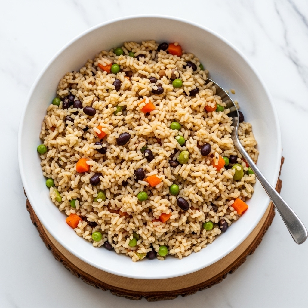 A large white bowl filled with cooked rice mixed with small pieces of orange carrot, yellow corn, green peas, and black beans, creating a colorful, textured mix. The rice grains appear fluffy and lightly coated with a reddish-brown seasoning. A silver spoon rests inside the bowl on the right side. The bowl sits on a wooden round board, all placed on a white marbled surface with a blurred decorative object in the background. photo taken with an iphone --ar 4:5 --v 7