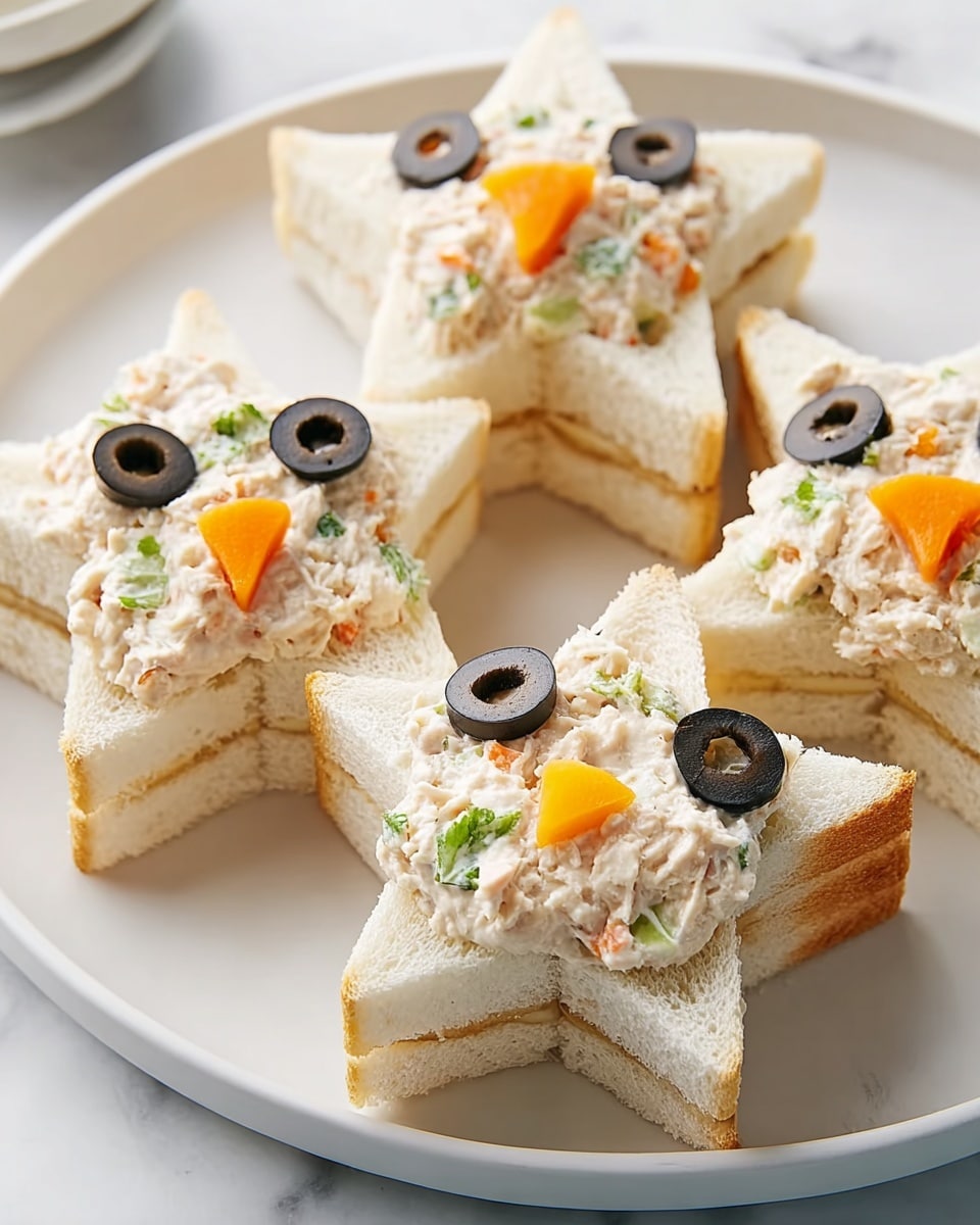 The image shows four star-shaped sandwiches on a white plate, each made from two layers of soft white bread with filling in between and on top. The filling is creamy with small bits of orange carrot and green herbs mixed into a beige base. On top of each sandwich, two black olive slices are placed to resemble eyes, and a small star-shaped carrot piece is placed below the eyes, resembling a nose or decoration. The background has a white marbled texture, and the overall look is clean and simple, focusing on the cute star-shaped snacks. photo taken with an iphone --ar 4:5 --v 7