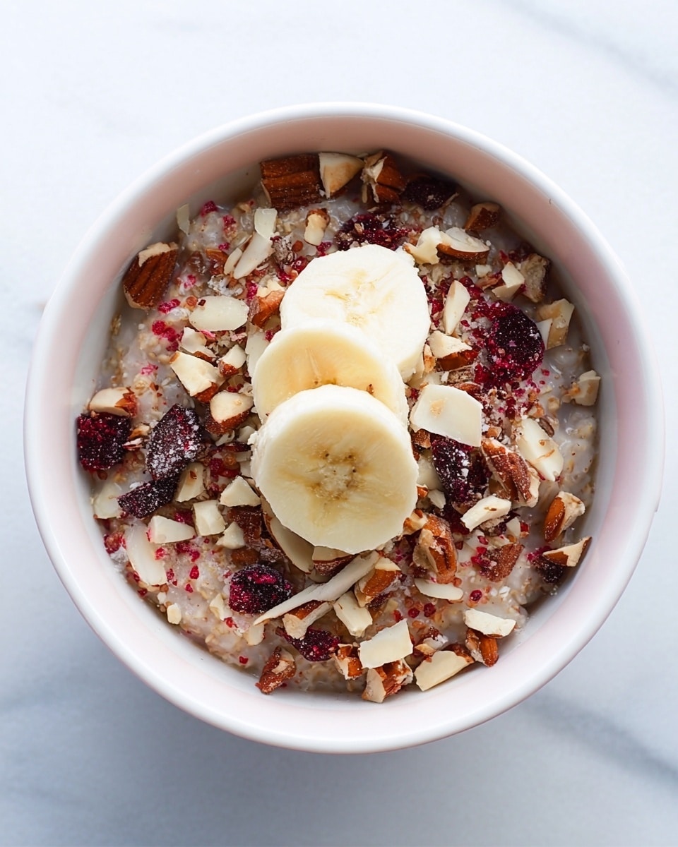 A close-up view of a bowl filled with a layered breakfast mixture. At the bottom, there is a creamy oatmeal base, light brown in color with a soft texture. On top of that, a layer of evenly chopped pieces of red apple, dark brown raisins, and small crunchy walnut bits are scattered throughout. The topmost layer consists of thin, round, pale yellow slices of banana arranged in the center, sprinkled lightly with ground cinnamon and additional walnut pieces. The bowl itself is white with a light lavender inside, set on a white marbled surface. photo taken with an iphone --ar 4:5 --v 7