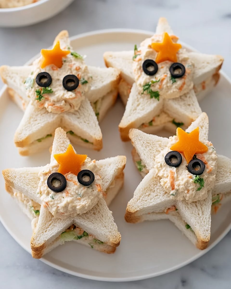 Four star-shaped sandwiches are arranged on a white plate over a white marbled surface. Each sandwich has three layers of soft white bread cut into stars. The top layer is hollowed out, holding a soft, creamy chicken salad mixed with small pieces of green herbs and orange carrot bits. On top of the salad, two round black olive slices sit as eyes, and a small orange carrot star is placed as a nose, giving a cute face-like look to each sandwich. Photo taken with an iphone --ar 4:5 --v 7