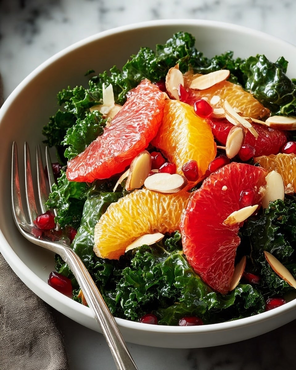 A white bowl filled with a fresh kale salad shows three layers: the base layer is dark green kale leaves with a rough texture, the middle layer has bright orange and deep pink grapefruit and orange slices with a juicy, translucent look, and the top layer is sprinkled with thin, oval-shaped light brown almond slices and small, shiny red pomegranate seeds. A silver fork rests on the left side of the bowl against a white marbled surface. Photo taken with an iphone --ar 4:5 --v 7