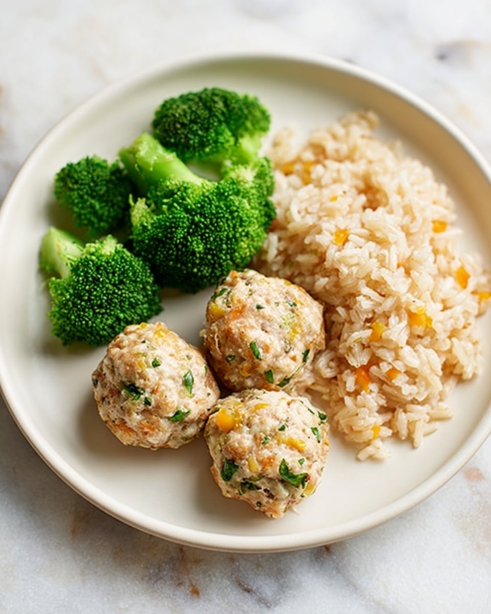 A white plate holds a simple meal with three main parts: on the left side is a small pile of light brown cooked rice with a soft texture; behind the rice, bright green broccoli florets with a fresh, slightly rough surface are arranged; on the right side of the plate, three round meatballs with a speckled look of green herbs and bits of orange carrot are placed close together, showing a slightly moist and tender texture. The plate sits on a white marbled surface. photo taken with an iphone --ar 4:5 --v 7