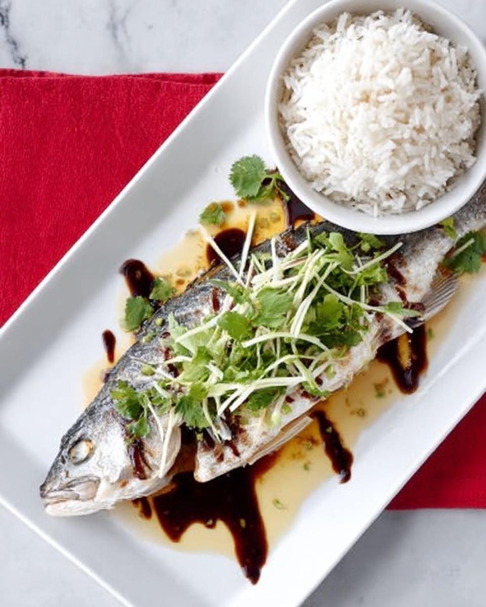 The image shows a cooked whole fish placed diagonally on a white rectangular plate with mild grill marks on the silver skin. The fish is topped with thin yellow ginger strips, green cilantro leaves, and thin sliced green onions, with dark brown sauce drizzled in lines over and around it. Next to the fish on the same plate, there is a small white bowl filled with fluffy white rice. The plate is set on a white marbled surface with a red cloth partially visible on the left side. Photo taken with an iphone --ar 4:5 --v 7