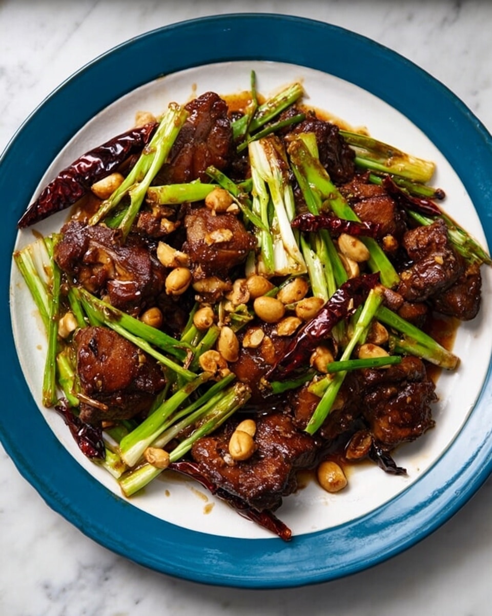 The dish shows several pieces of dark brown, glazed chicken wings spread across a large white oval plate. On top and around the chicken, there are light green and white spring onion sticks positioned in a scattered way. Small golden-brown peanuts are sprinkled over the chicken and onions, adding texture. Dried red chili peppers are mixed in among the chicken, adding deep red color contrast. The plate is placed on a white marbled surface. Photo taken with an iphone --ar 4:5 --v 7