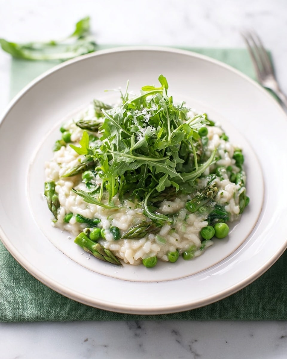 A white plate holds a creamy risotto mixed with bright green peas and asparagus pieces, creating a fresh and colorful layer. On top of this main layer, a small pile of vibrant green arugula leaves adds height and texture, with a few thin shavings of white cheese scattered gently over the dish. The plate sits on a white marbled surface, with a soft light making the colors pop. Photo taken with an iphone --ar 4:5 --v 7