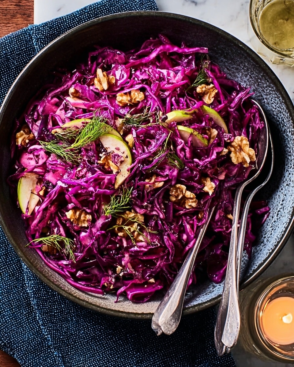 A close-up view of a dark bowl filled with a colorful salad made of bright purple shredded cabbage that forms the main layer, mixed with thin green apple slices and scattered walnut pieces on top, adding texture and warmth. There are also small sprigs of fresh green dill sprinkled throughout, giving a touch of freshness and contrast. Two silver serving spoons rest inside the bowl on the right side, and the bowl sits on a white marbled surface with a navy blue textured cloth partially under it. A lit candle in a small glass holder is placed near the bottom right corner. Photo taken with an iphone --ar 4:5 --v 7