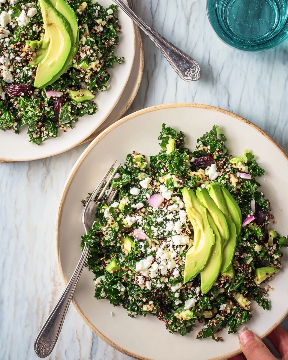 The image shows two white plates of salad on a white marbled surface. Each plate has a bed of dark green kale mixed with light-colored quinoa, small pieces of green celery, chopped red onions, and dark red raisins. On top of the salad, there are several slices of bright green avocado, fanned out neatly in the center. White crumbles of cheese are scattered over the avocado and salad. Each plate has a silver fork resting on its edge. The overall look is fresh and colorful, with a mix of green, white, red, and beige tones. photo taken with an iphone --ar 4:5 --v 7
