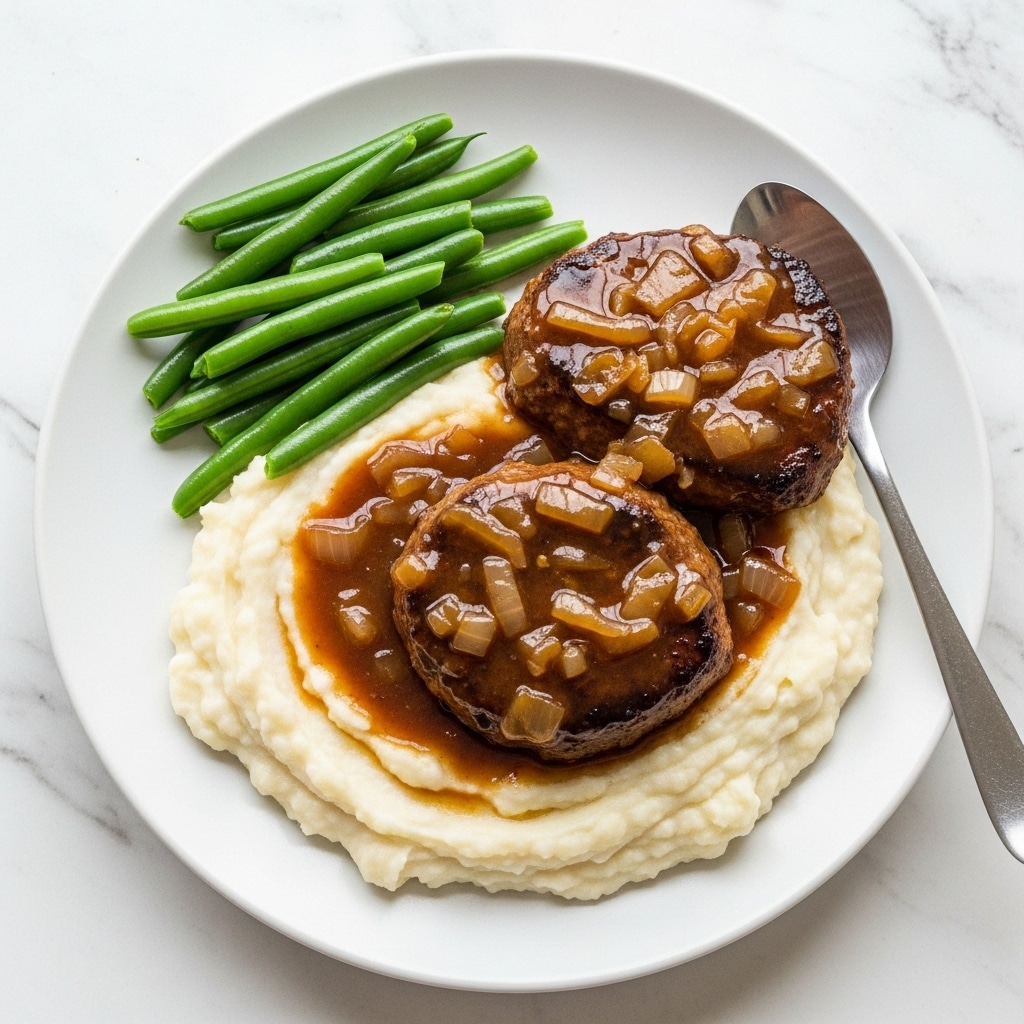 A white plate sits on a white marbled surface holding a comforting meal with three main layers. The bottom layer is a bed of creamy mashed potatoes, smooth and slightly textured with small specks, spread evenly across the plate. On top of the mashed potatoes, there is a pan-fried Salisbury steak with a rich brown color and a slightly seared texture. Covering the steak is a thick, glossy brown gravy with visible cooked onion pieces, adding shine and moisture. On the side of the plate, there is a neat pile of bright green steamed green beans. A silver spoon rests on the plate edge next to the mashed potatoes and gravy. photo taken with an iphone --ar 4:5 --v 7