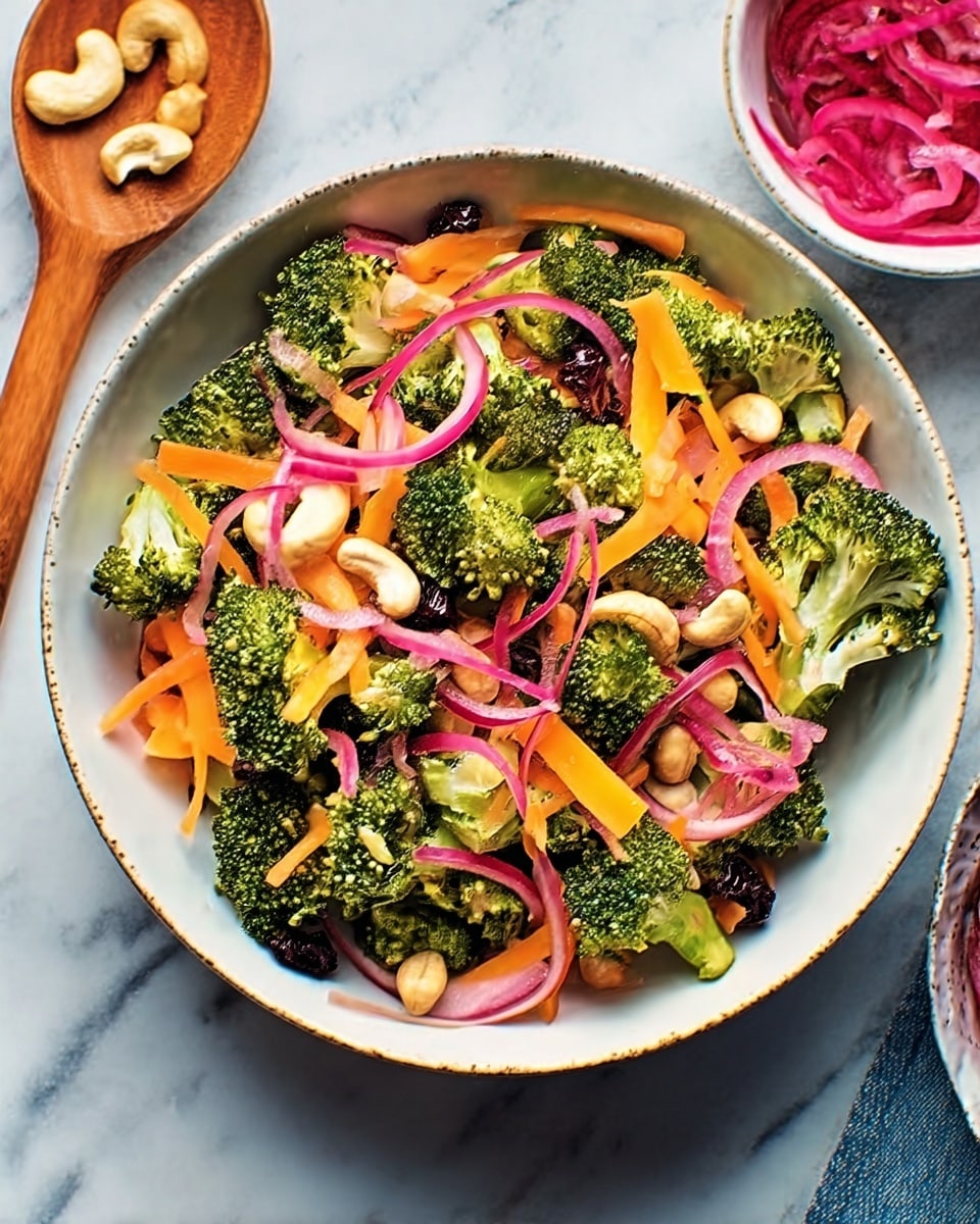 A white bowl on a white marbled surface holds a colorful salad with several layers. The base layer is dark green broccoli florets cut into small pieces, spread around the bowl. On top of the broccoli are thin, curly orange carrot ribbons laid loosely. Bright pink pickled onion rings are scattered over the carrots, adding a pop of color. Small white cashew nuts are mixed throughout, along with some kidney beans for extra texture. The salad looks fresh and vibrant with a mix of rough, smooth, and crunchy textures. Photo taken with an iphone --ar 4:5 --v 7